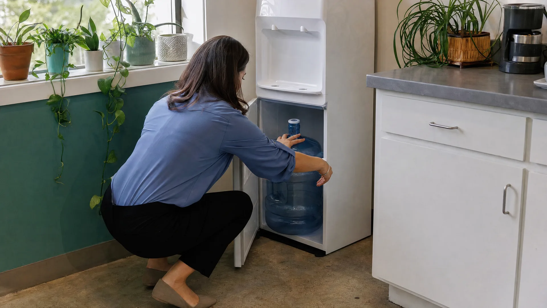 Office manager crouching to load a 5-gallon jug into a bottom-load cooler