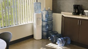 Full and empty 5-gallon jugs stacked beside a bottle-top cooler in a break room