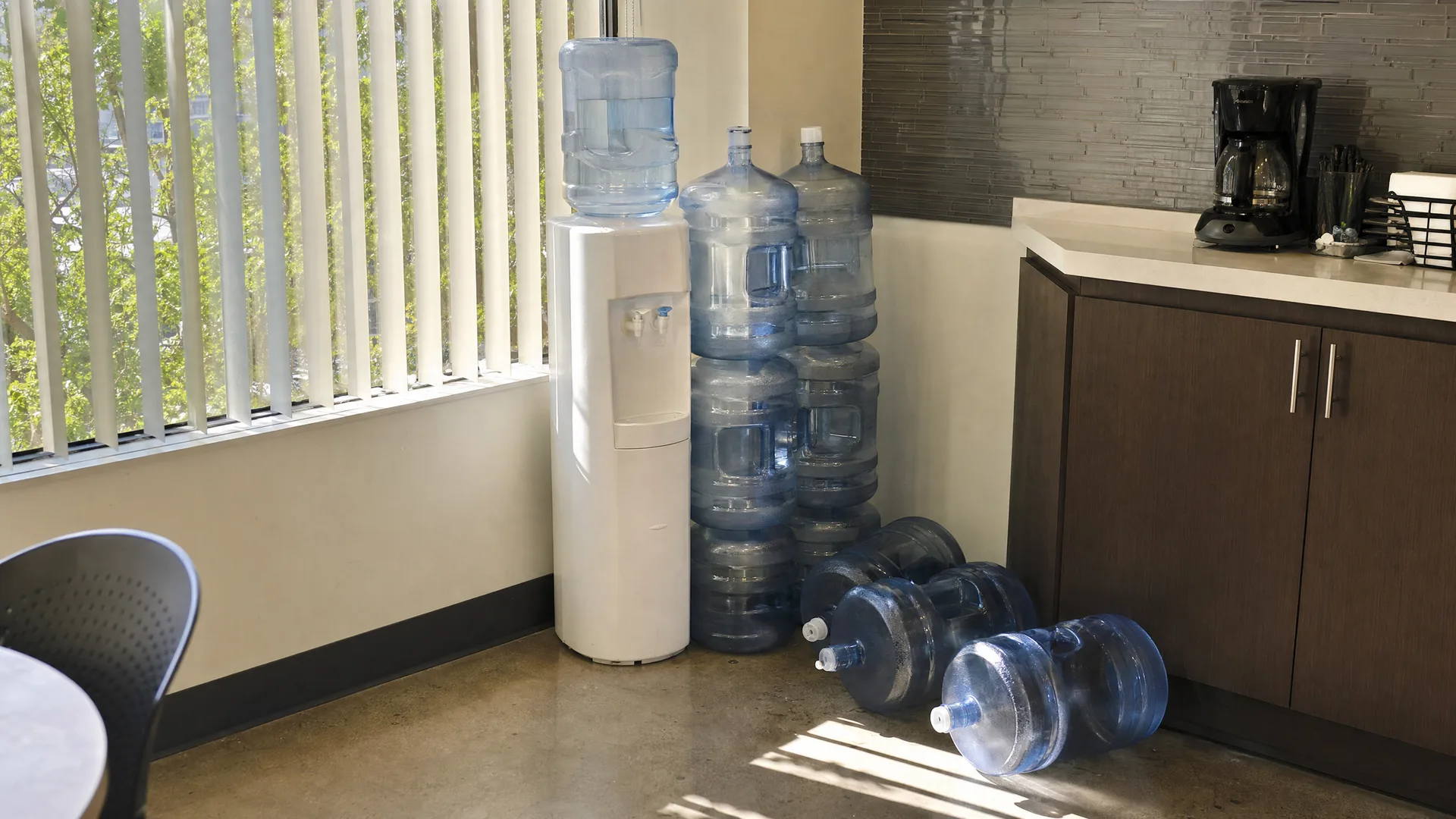 Full and empty 5-gallon jugs stacked beside a bottle-top cooler in a break room